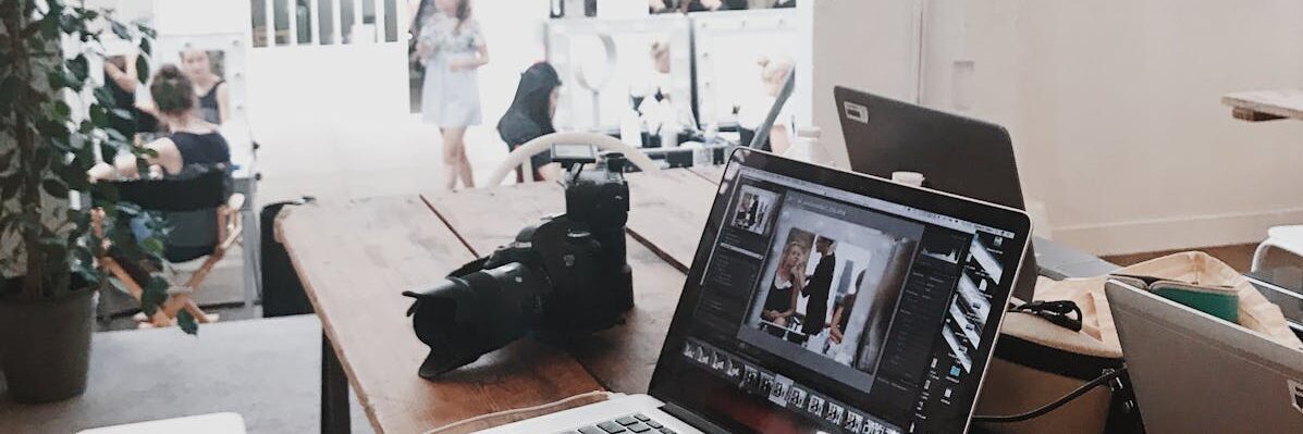A bright, modern workspace featuring laptops, a camera, and a drawing tablet in an indoor office.